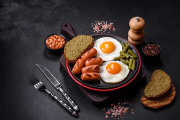 Tasty English breakfast of fried eggs, beans, asparagus, sausages with spices and herbs