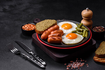 Tasty English breakfast of fried eggs, beans, asparagus, sausages with spices and herbs