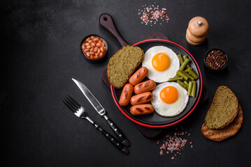 Tasty English breakfast of fried eggs, beans, asparagus, sausages with spices and herbs