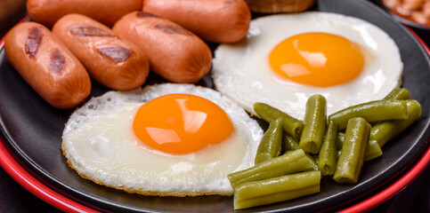 Tasty English breakfast of fried eggs, beans, asparagus, sausages with spices and herbs
