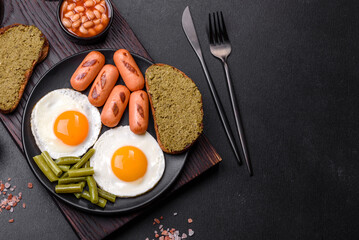 Tasty English breakfast of fried eggs, beans, asparagus, sausages with spices and herbs