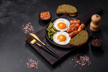 Tasty English breakfast of fried eggs, beans, asparagus, sausages with spices and herbs