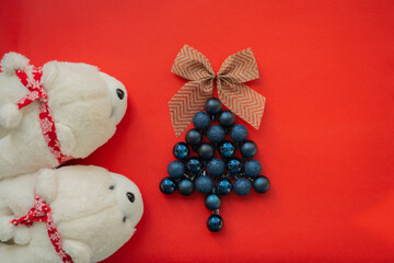 White bear slippers and a Christmas tree of dark blue Christmas balls on a red background. Red and yellow bow on top of the Christmas tree. Matte, glossy and glitter balls. New Year's decoration - Powered by Adobe