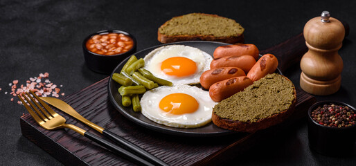 Tasty English breakfast of fried eggs, beans, asparagus, sausages with spices and herbs