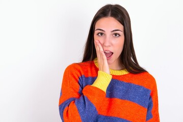 Shocked Young caucasian woman wearing colorful knitted sweater over white background looks with great surprisment being very stunned, astonished with unexpected news, Facial expressions concept.