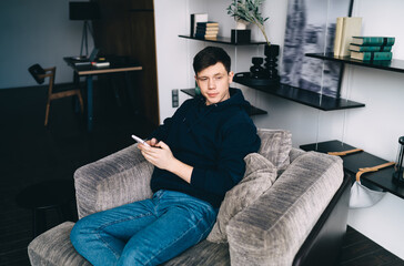 Young man sitting with smartphone on sofa in living room