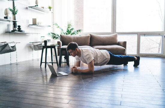 Concentrated man doing forearm plank exercise while watching sport lesson on laptop - Powered by Adobe