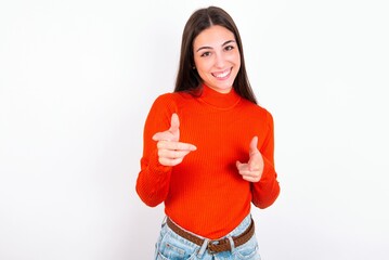 Young caucasian woman wearing red sweater over white background directs fingers at camera selects...