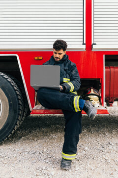Hispanic fireman using laptop near fire engine