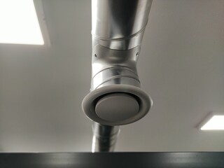 Extractor hood in a public toilet. Round metal pipe with gray air extractor. Engineering ventilation systems. Galvanized pipes under the ceiling of the room. Plastic round tip.