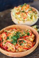 Fried cabbage in a wooden bowl on the table. Decoration of sweet pepper and green dill.