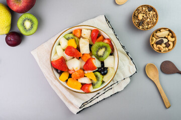 Fresh fruit salad in a bowl. Multicolored and tropical fruits. Pineapple, mango, grape, strawberry, papaya, melon, kiwi. Additional with chestnuts and granola. Top view. Selective focus