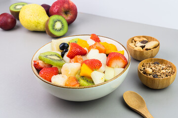 Fresh fruit salad in a bowl. Multicolored and tropical fruits. Pineapple, mango, grape, strawberry, papaya, melon, kiwi. Additional with chestnuts and granola. Selective focus