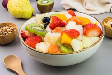 Fresh fruit salad in a bowl. Multicolored and tropical fruits. Pineapple, mango, grape, strawberry, papaya, melon, kiwi. Additional with chestnuts and granola. Selective focus