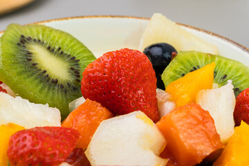 Fresh fruit salad in a bowl. Multicolored and tropical fruits. Pineapple, mango, grape, strawberry, papaya, melon, kiwi. Additional with chestnuts and granola. Selective focus