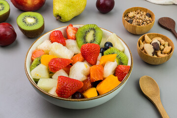 Fresh fruit salad in a bowl. Multicolored and tropical fruits. Pineapple, mango, grape, strawberry, papaya, melon, kiwi. Additional with chestnuts and granola. Selective focus