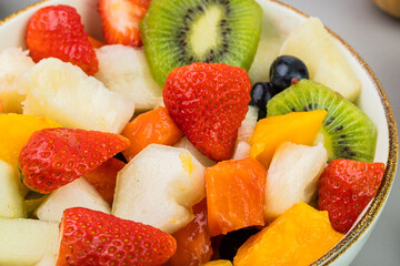 Fresh fruit salad in a bowl. Multicolored and tropical fruits. Pineapple, mango, grape, strawberry, papaya, melon, kiwi. Additional with chestnuts and granola. Selective focus