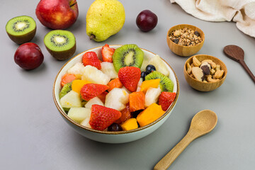 Fresh fruit salad in a bowl. Multicolored and tropical fruits. Pineapple, mango, grape, strawberry, papaya, melon, kiwi. Additional with chestnuts and granola. Selective focus