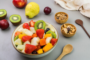 Fresh fruit salad in a bowl. Multicolored and tropical fruits. Pineapple, mango, grape, strawberry, papaya, melon, kiwi. Additional with chestnuts and granola. Selective focus