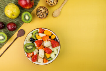 Fresh fruit salad in a bowl. Multicolored and tropical fruits. Pineapple, mango, grape, strawberry, papaya, melon, kiwi. Additional with chestnuts and granola. Top view. Selective focus