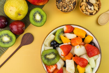 Fresh fruit salad in a bowl. Multicolored and tropical fruits. Pineapple, mango, grape, strawberry, papaya, melon, kiwi. Additional with chestnuts and granola. Top view. Selective focus