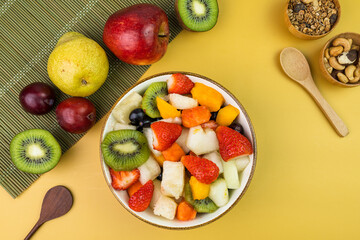 Fresh fruit salad in a bowl. Multicolored and tropical fruits. Pineapple, mango, grape, strawberry, papaya, melon, kiwi. Additional with chestnuts and granola. Top view. Selective focus