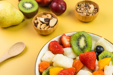 Fresh fruit salad in a bowl. Multicolored and tropical fruits. Pineapple, mango, grape, strawberry, papaya, melon, kiwi. Additional with chestnuts and granola. Selective focus