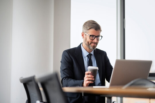 Executive businessman having a coffee and using laptop while working at the office