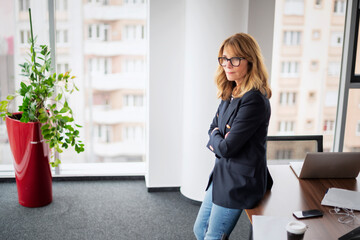 Executive business woman deep in thought while standing with folded arms in a modern office