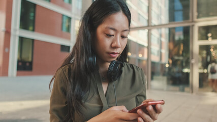 Young laughing woman freelancer in headphones works uses cellphone