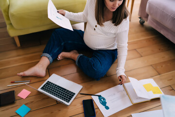 Pregnant woman working on project with papers notebook and laptop