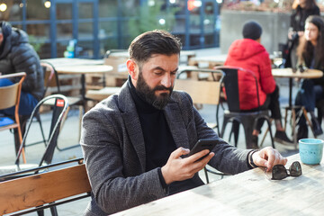 brutal bearded middle-aged man in a street cafe uses a mobile phone