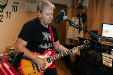 Concentrated male musician playing guitar near modern recording equipment