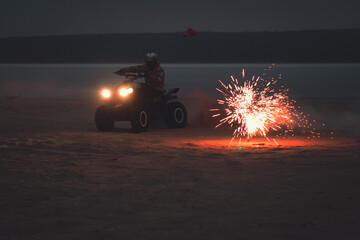Athlete on a quad bike rides at night on a sandy beach with fireworks © Елена Вырыпаева