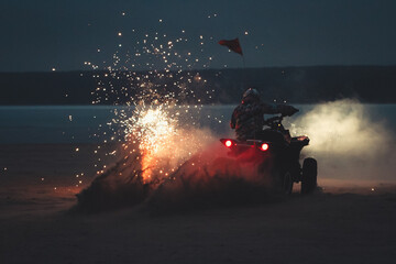 Athlete on a quad bike rides at night on a sandy beach with fireworks