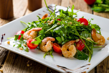 Arugula with shrimps and tomatoes on white plate macro close up, wooden table