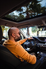 bald bearded middle-aged man drives a car