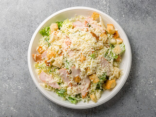 Salad caesar with chicken on white plate top view on grey table
