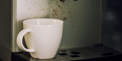 White cup stands at dirty coffee machine counter closeup. Empty cup for coffee at home or office.