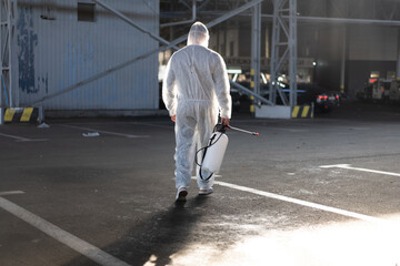 Man dressed white protective overalls spraying surface antibacterial sanitizer sprayer during quarantine