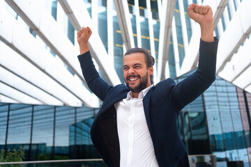 Excited young businessman in suit celebrating victory arms raised