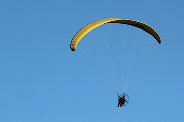 Paragliding in a blue sky, pilot controls motorized flying machine