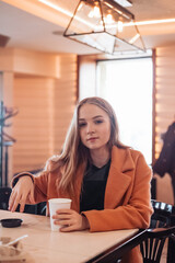 beautiful young woman with a glass of takeaway coffee sits in a cafe