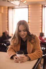 beautiful young woman with a glass of takeaway coffee sits in a cafe