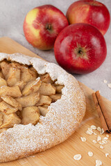 On a wooden board apple galette with oatmeal, cinnamon and red apples in the background.
