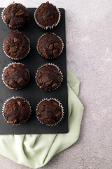 On a gray table are chocolate muffins on a dark board.