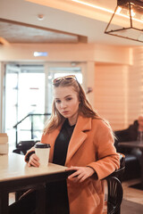 beautiful young woman with a cup of takeaway coffee and donuts sits in a cafe