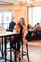 beautiful young woman with a cup of takeaway coffee and donuts sits in a cafe