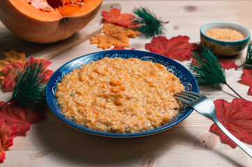 Close up view of pumpkin risotto, with pumpkin, bowl of rice and maple leaves over a wooden table