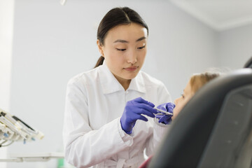 Side view of smiling pretty asian doctor in white uniform and gloves, making examination or curing...